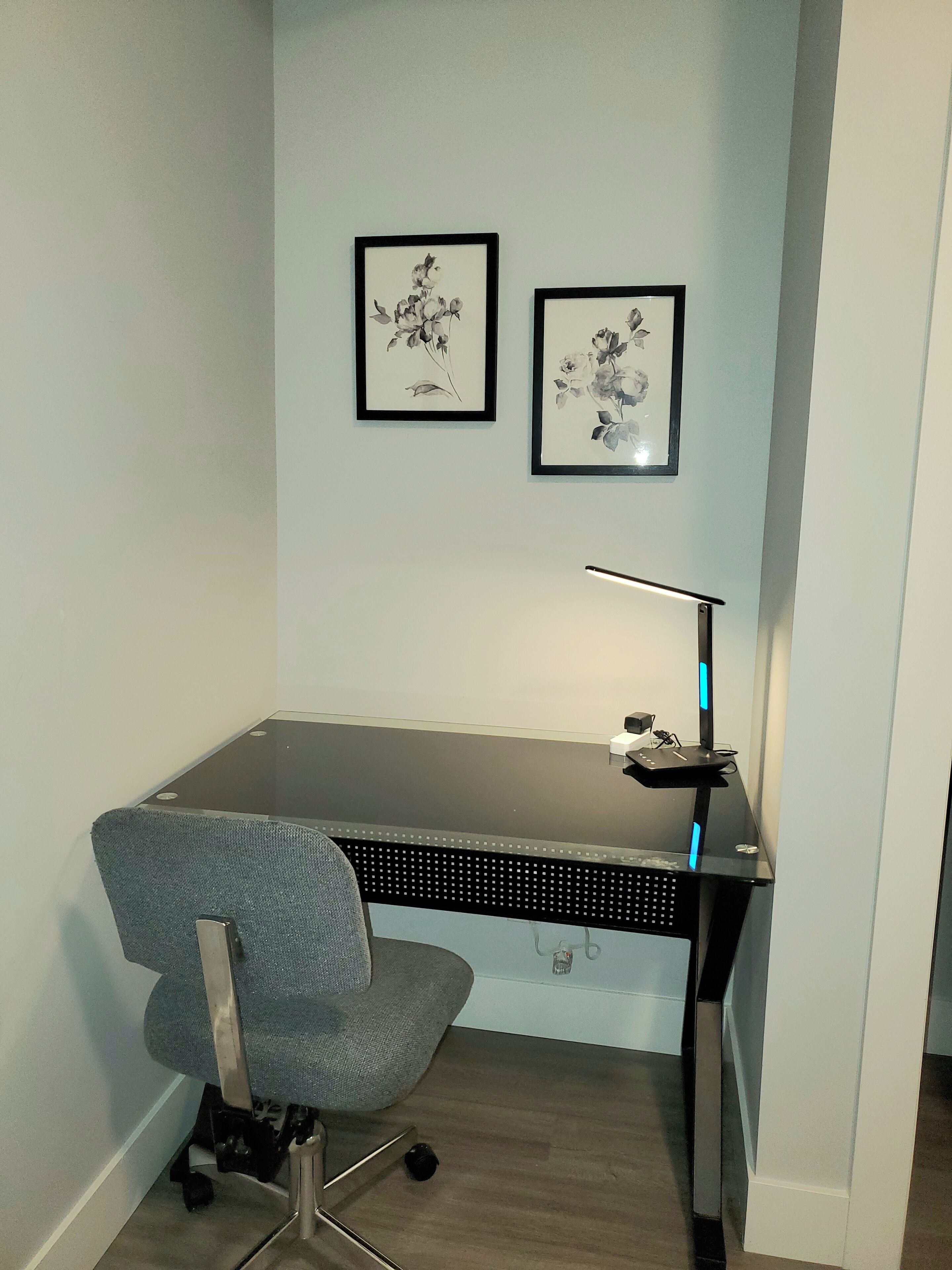 Ett hörnkontor med ett skrivbord, en stol och två inramade konstverk med blommotiv på väggen.
