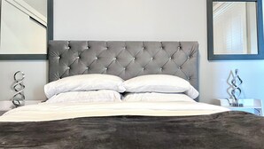 A neatly made bed with a tufted headboard, two bedside tables with decorative metal sculptures, and two wall-mounted mirrors. - Stunning Ocean View 1 BDR Private Entry Suite (Colwood)