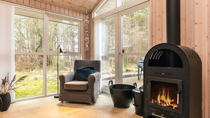 Una habitación acogedora con chimenea, un sillón cómodo y ventanas amplias con vistas al exterior.