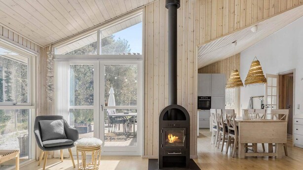 Un amplio salón con chimenea, piso de madera y grandes ventanales con vistas al exterior.