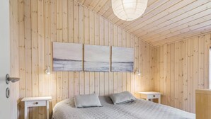 Un dormitorio con pared de paneles de madera, cama con cubrecama gris, dos mesitas de noche y una lámpara en el techo.