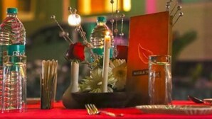 Une table dressée avec une nappe rouge, agrémentée d’une bouteille d’eau, d’une bougie, d’une rose et d’un menu.