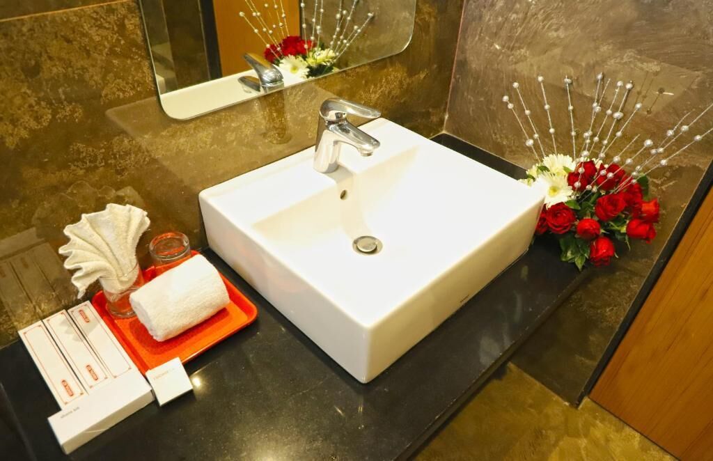 A bathroom with a white sink, a mirror, and a decorative arrangement of red roses.