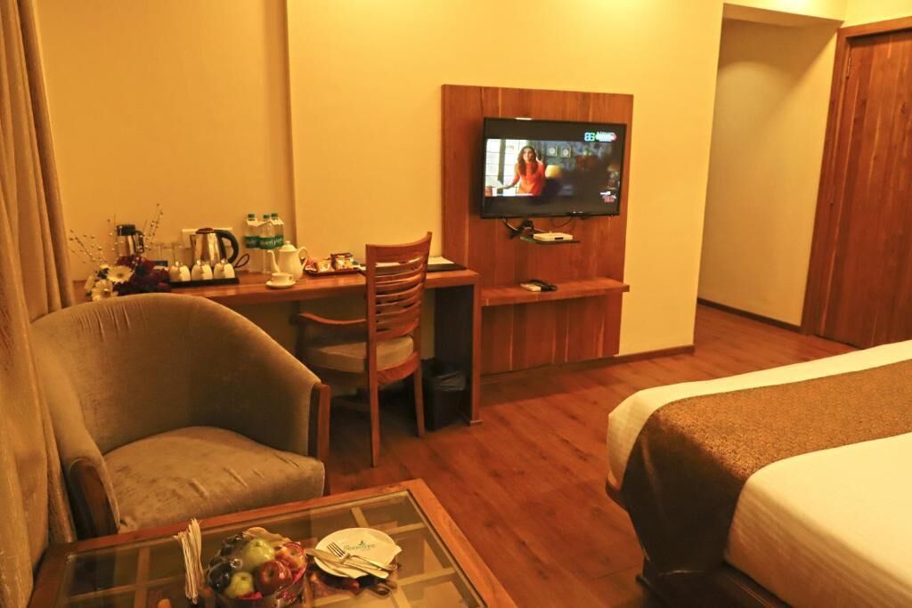 A hotel room with a bed, a desk with a television, a chair, a coffee table, and a small table with a fruit bowl.