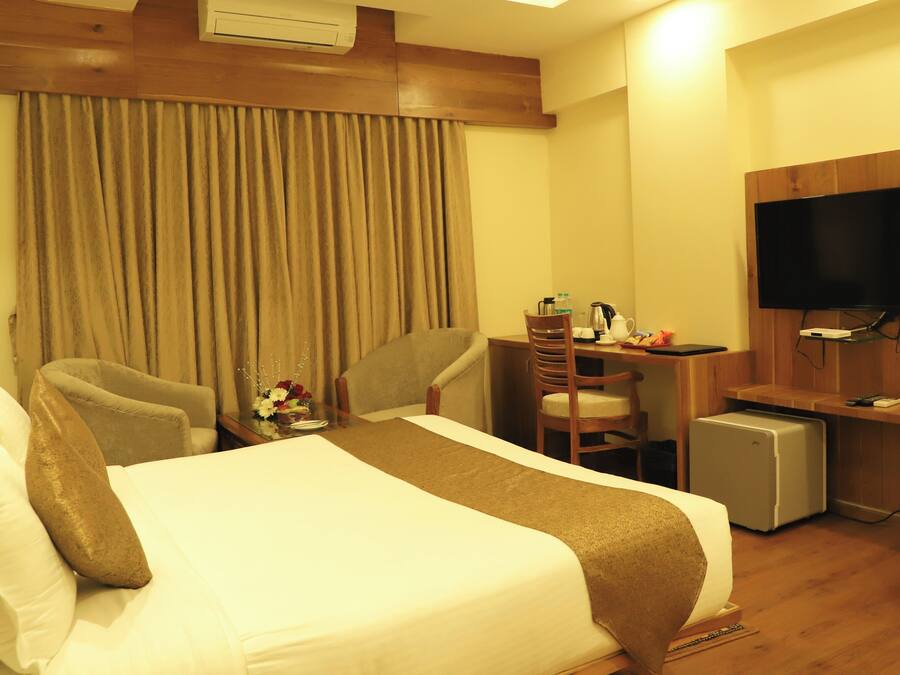 Habitación de hotel con cama, escritorio, silla, televisión y un refrigerador pequeño.