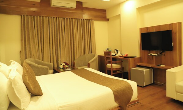 Habitación de hotel con cama, escritorio, silla, televisión y un refrigerador pequeño.