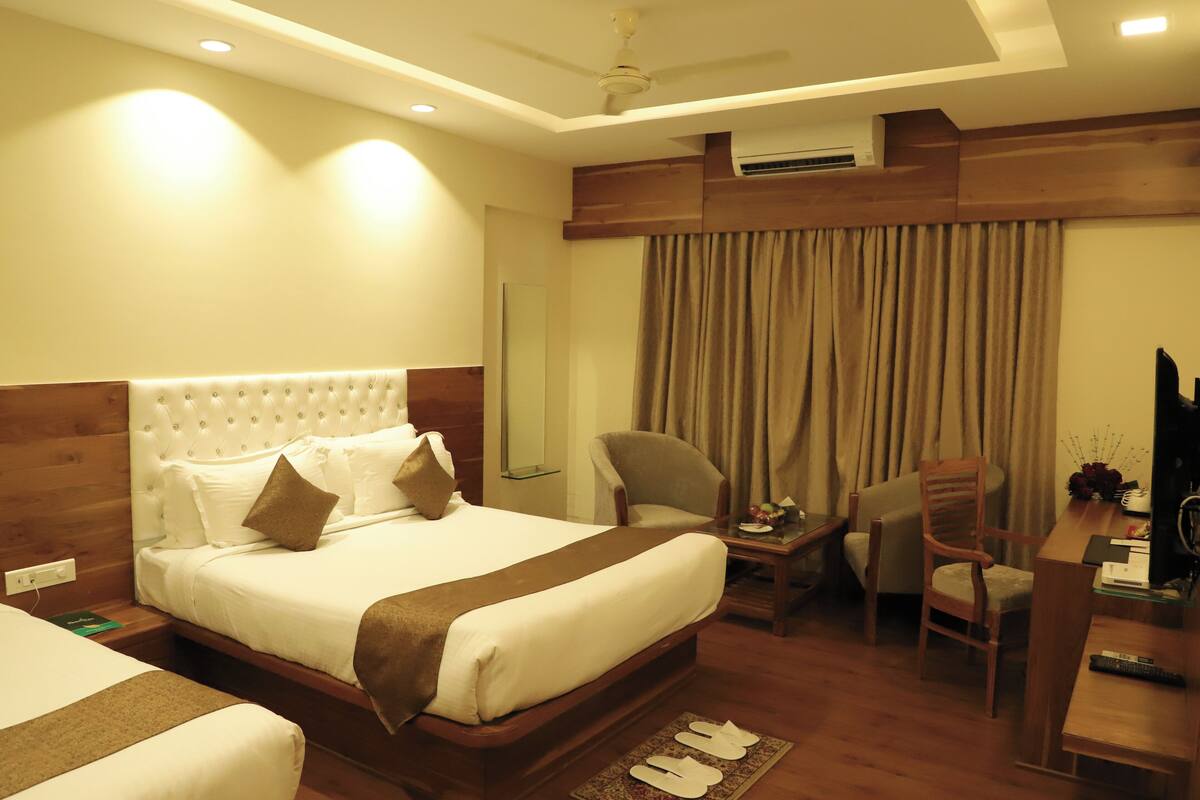 A hotel room with a large bed, two armchairs, a desk with a computer, and a TV.