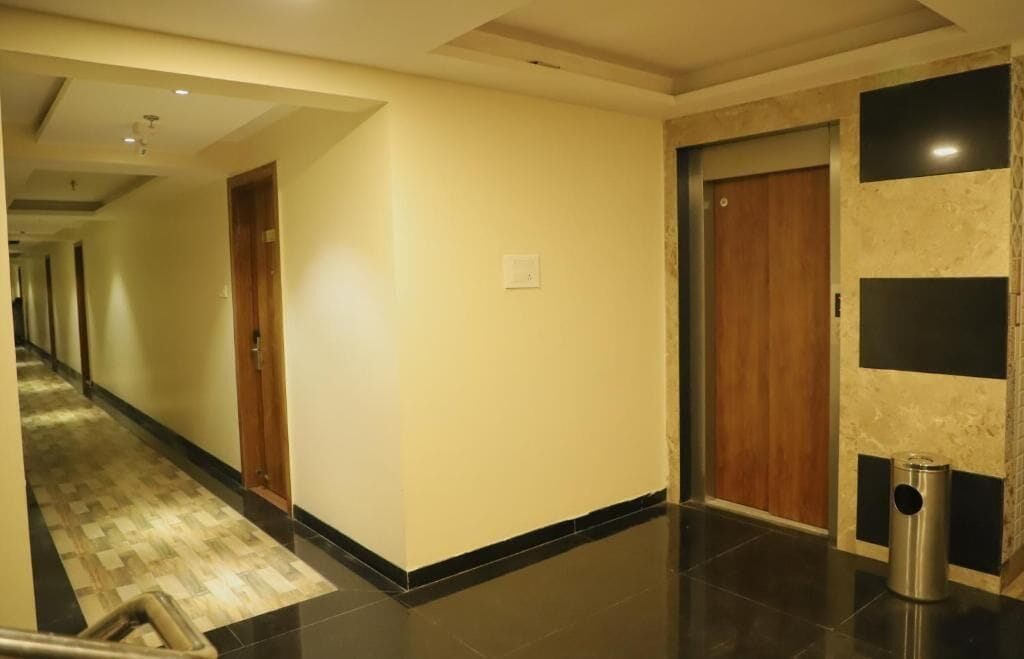 A hotel hallway with a checkered floor, a trash bin, and a wooden door.