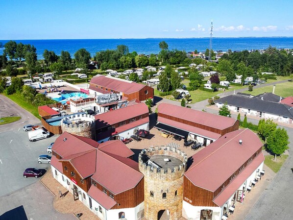 A castle-like building with a central tower, surrounded by smaller structures with red roofs, set against a backdrop of a coastal area with clear skies. - 6 Person Holiday Park Home in Otterup (Otterup)