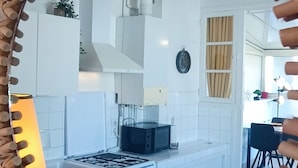 A modern kitchen with white cabinets, a gas stove, and a hanging light fixture. - Rosemonde  Terrasse, calme  esprit village à La Chaume (Les Sables-d´Olonne)