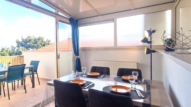 A dining area with a table set for four, a view of the outdoors, and a decorative metal sculpture on the wall. - Rosemonde  Terrasse, calme  esprit village à La Chaume (Les Sables-d´Olonne)