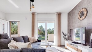 Una sala de estar moderna con un sofá gris, un televisor de pantalla plana y un ventanal con cortinas.