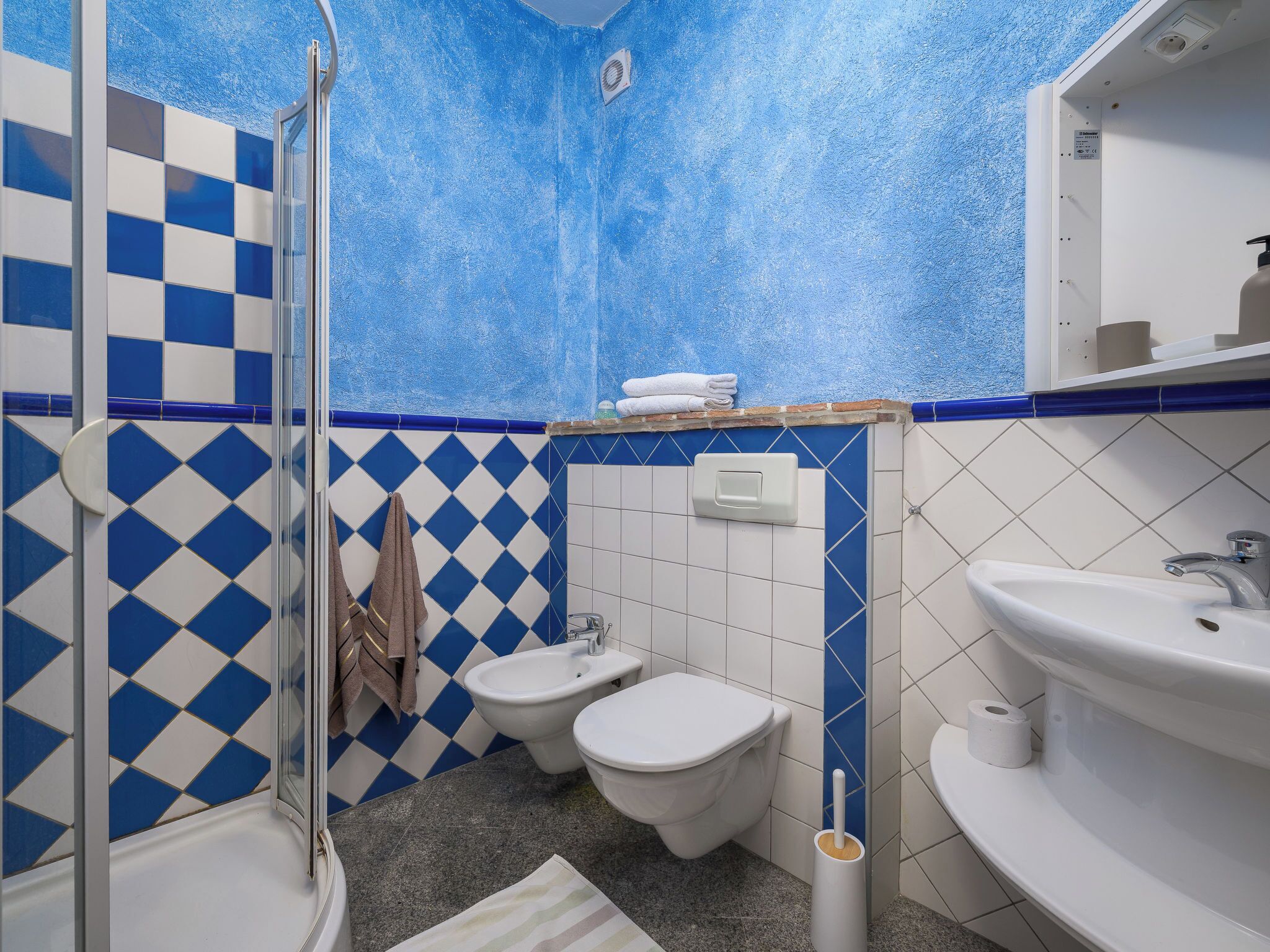 Une salle de bain avec un mur à carreaux bleus et blancs, une douche, un bidet, des toilettes et un lavabo.