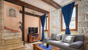 A cozy living room with a stone wall, a wooden staircase, a television on a wooden stand, a sofa, and a coffee table. - Vista 2 by Interhome (Vrsar)