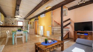 A spacious living area with a wooden staircase, a dining table with chairs, a sofa, and a television on a wooden stand. - Vista 2 by Interhome (Vrsar)
