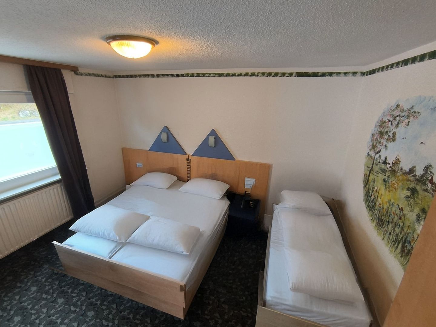 A hotel room with a bed, a bench, a nightstand, a painting, and a window with curtains.