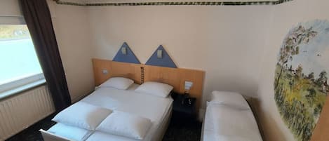 Hotellihuone, jossa on sänky, penkki, yöpöytä, taulu ja ikkuna, jossa on verhot.