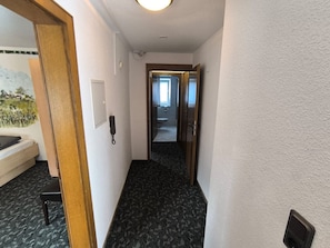 A hotel hallway with a carpeted floor, a telephone, and a door leading to a bathroom.