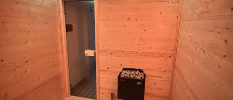 Un sauna con paredes de madera, una puerta, un cubo y una caja de astillas.