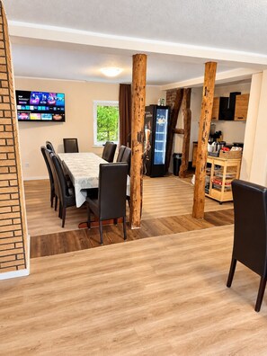 A dining area with a table and chairs, a television mounted on the wall, and a refrigerator with a beverage dispenser.
