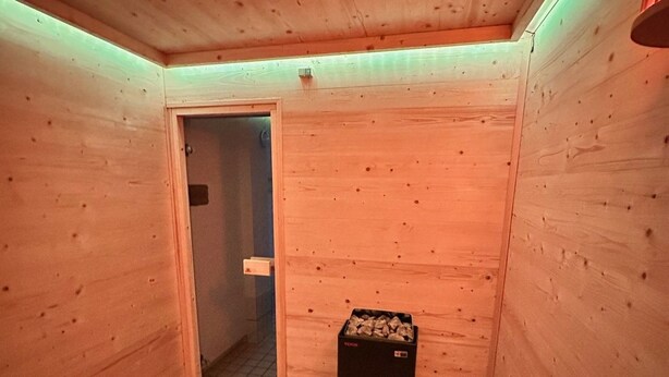 Et saunaområde med trævægge, en dør, en spand og en kasse med træflis.