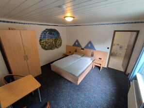 Une chambre d’hôtel avec un lit, un bureau, une armoire et une salle de bain, visibles à travers une porte ouverte.