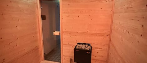 A sauna room with wooden walls, a door, a bucket, and a box of wood chips.
