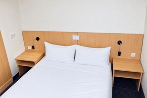 A hotel room with a single bed, two bedside tables, and two wall-mounted lamps.