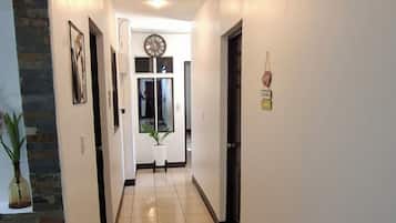 Um corredor com piso ladrilhado, um relógio e uma porta no final.