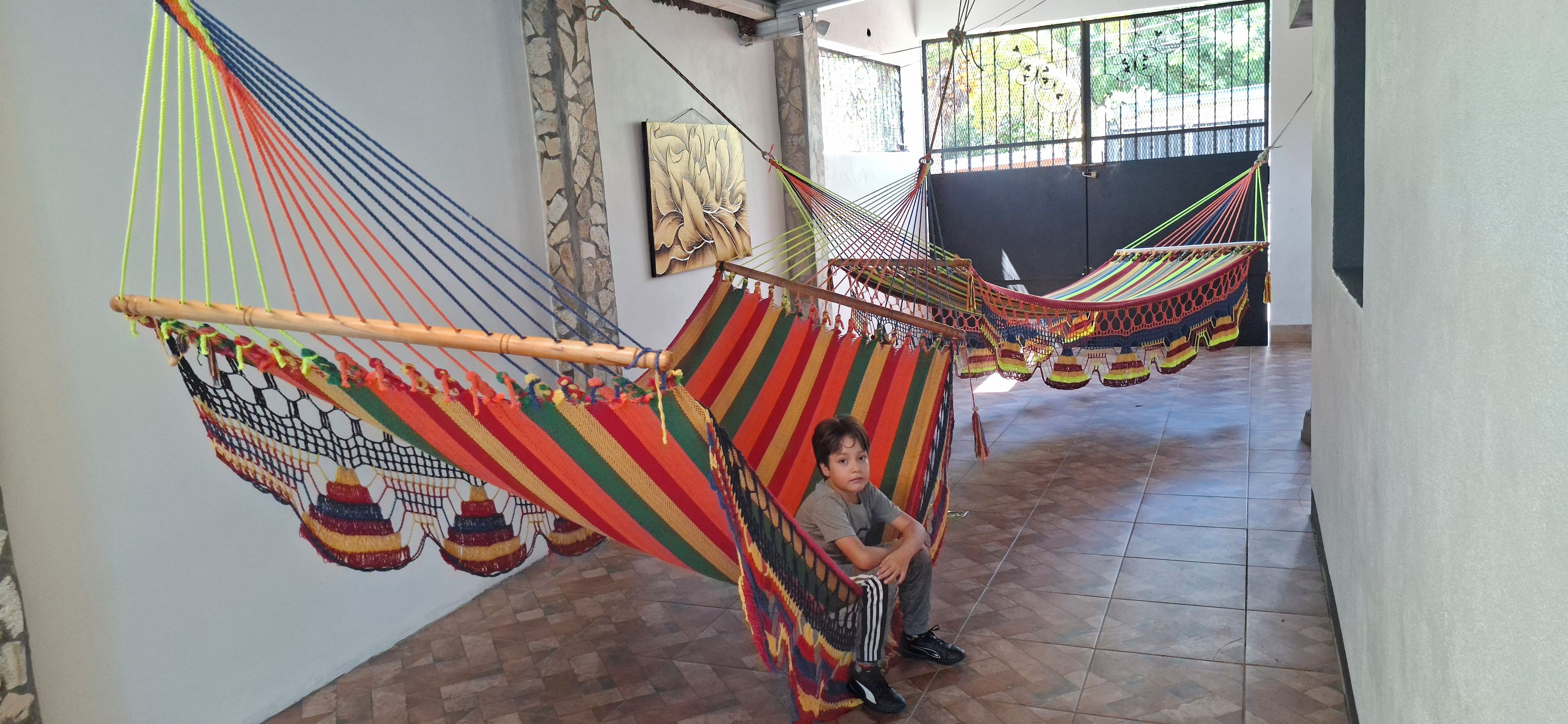 A child sitting in a hammock in a hallway with tiled flooring and a stone wall.