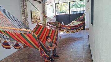 A child sitting in a hammock in a hallway with tiled flooring and a stone wall.
