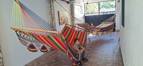 A child sitting in a hammock in a hallway with tiled flooring and a stone wall.
