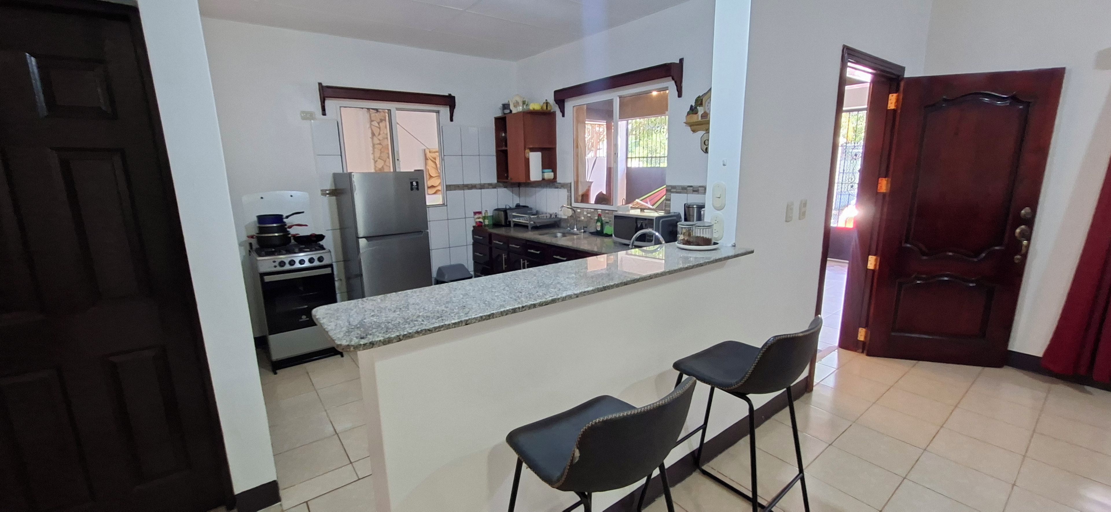 A kitchen with a refrigerator, stove, and bar stools.