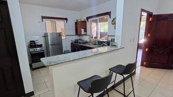 A kitchen with a refrigerator, stove, and bar stools.