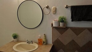 Un bagno con uno specchio rotondo, un lavabo, un porta asciugamani, una piccola pianta in vaso e un fiorile a parete.