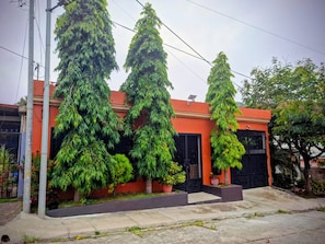 Un edificio residencial con fachada roja, portones negros y tres árboles grandes en la parte frontal.