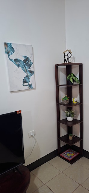 A room with a TV, a wall-mounted shelf with plants, and a painting.