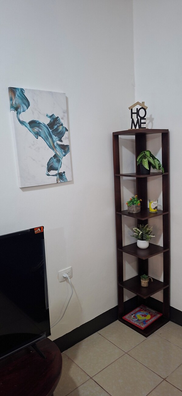 A room with a TV, a wall-mounted shelf with plants, and a painting.