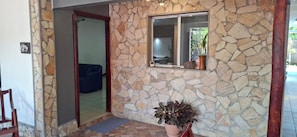 Entrada de paredes de piedra con planta en maceta, un sofá azul y una puerta que da al interior.
