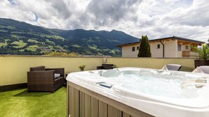 A hot tub with a wooden exterior, a grassy area, wicker furniture, and a mountain view in the background. - Apartment in Fugen Near Spieljoch Ski Lift (Fuegen)