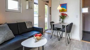 Un salon moderne avec un canapé, une table à manger et des chaises, une petite table ronde sur laquelle se trouve un saladier rempli de fruits, et un tableau accroché au mur.