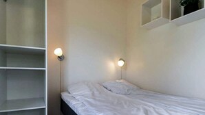 Une chambre avec un lit simple, une armoire et deux lampes fixées au mur.