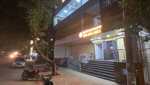 Un edificio de dos pisos con un letrero que dice "Motel Olive Leaves". Hay escalones que conducen a la entrada, y se ve un árbol en la acera.