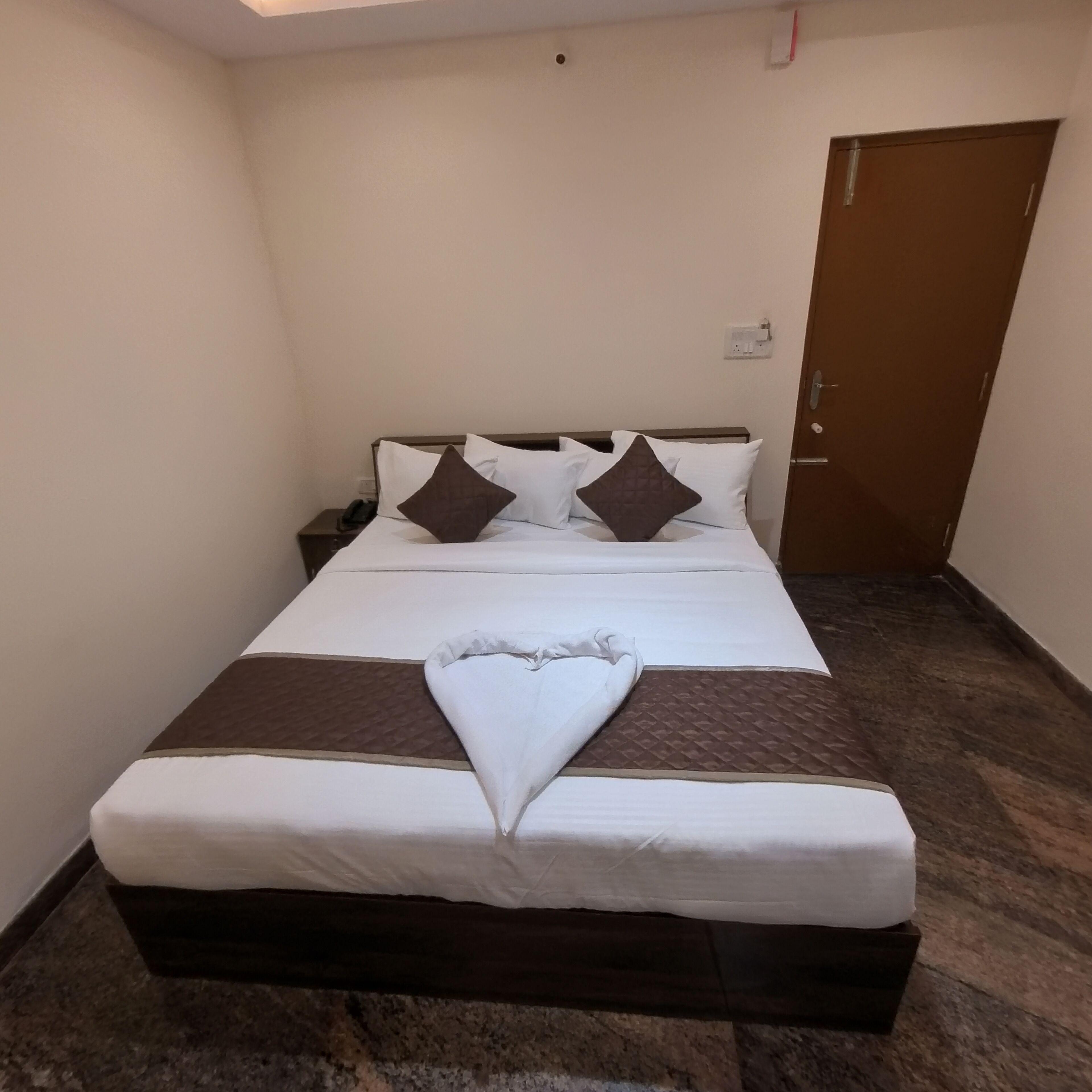 A neatly made bed with white and brown linens, a wooden headboard, and a brown accent pillow.