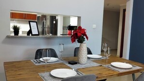 A dining area with a wooden table set for four, two chairs, a vase with red flowers, and a clock on the wall. - Charming and Comfortable 1BR | Jumeirah Bay X1| JLT (Dubai)