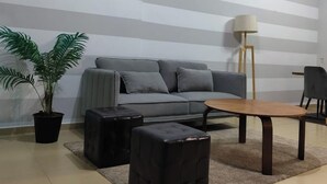 A living room with a grey sofa, two black ottomans, a wooden coffee table, a floor lamp, and a potted plant. - Charming and Comfortable 1BR | Jumeirah Bay X1| JLT (Dubai)