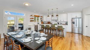 Una cocina moderna con armarios blancos, un refrigerador de acero inoxidable y un comedor preparado para seis personas.