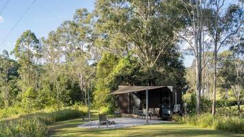 A secluded cabin with a covered outdoor seating area, surrounded by dense trees.