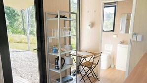 A compact kitchen with a built-in shelf unit, a foldable table, and a window overlooking a garden.
