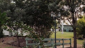A park with a wooden bench, a lamp post, and a building in the background. - Monto Magic by Tiny Away (Monto)